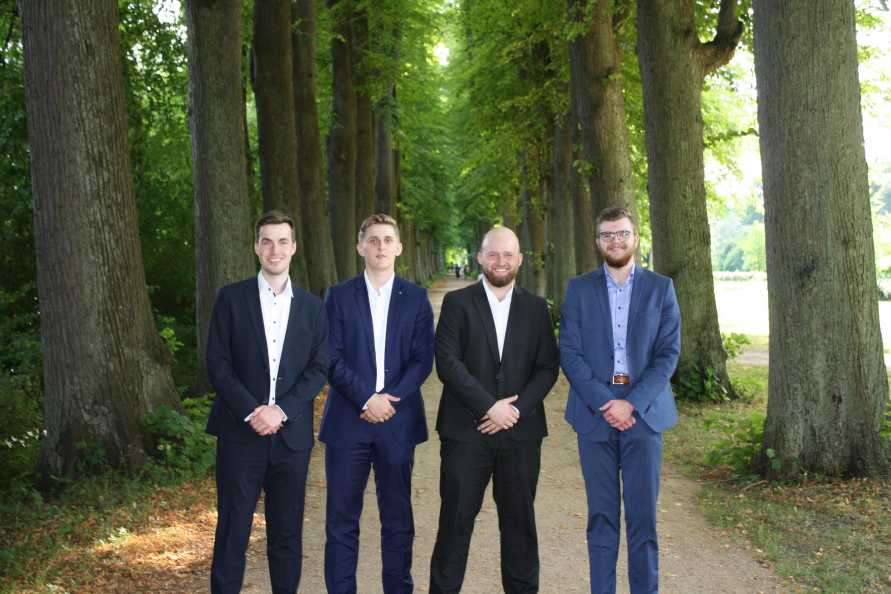 Das dritte Lehrjahr der Volksbank Eutin Vier junge Bankkaufleute in Anzügen auf einem Weg im Wald